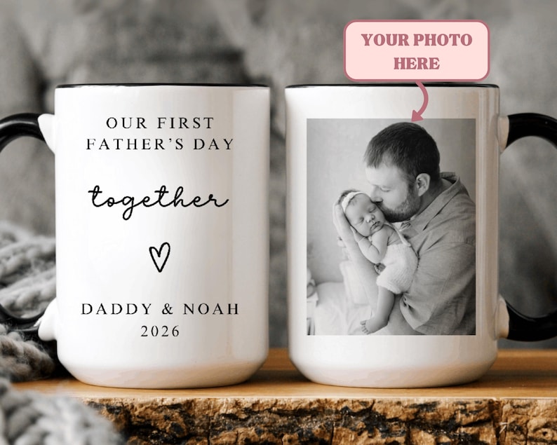May include: White ceramic mug with a black handle and rim. The mug features the text "OUR FIRST FATHER'S DAY together" with a heart symbol and "DADDY & NOAH 2026". The other side displays a black and white photo of a father and baby. The text "YOUR PHOTO HERE" is above the photo.