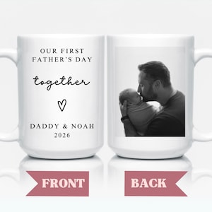 May include: White ceramic mug with the text "OUR FIRST FATHER'S DAY together" and "DADDY & NOAH 2026" on one side. The other side features a black and white photo of a father kissing a baby. A heart symbol is also present.