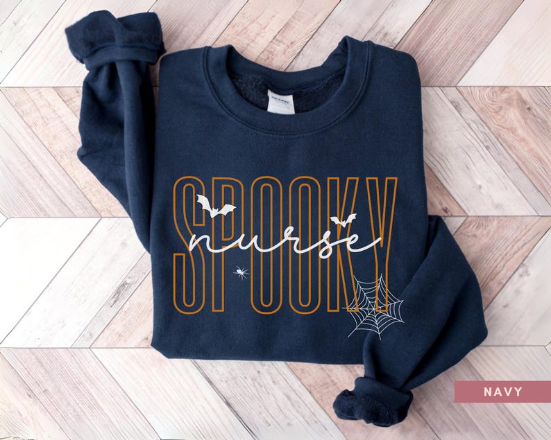 Puede incluir: Sudadera azul marino con las palabras "SPOOKY nurse" en naranja y blanco. El dise&ntilde;o incluye murci&eacute;lagos y una telara&ntilde;a, perfecto para Halloween. La sudadera es de cuello redondo.