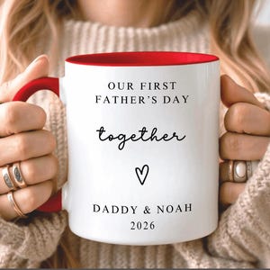May include: White ceramic mug with a red interior and handle. The mug features the text "OUR FIRST FATHER'S DAY together" with a heart symbol and the names "DADDY & NOAH" and the year "2026".