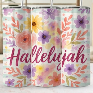 May include: A cylindrical tumbler with a metal straw featuring a watercolour floral pattern in shades of pink, yellow, and purple over light blue horizontal stripes. The word Hallelujah is printed in a dark magenta script font across the centre.