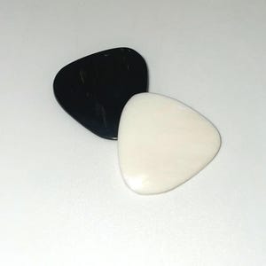 May include: Two guitar picks, one black and one white, are shown on a white surface.