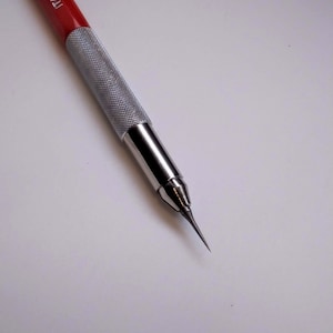 May include: A red and silver mechanical pencil with a fine point. The pencil has a textured silver grip and the words "ITALY KOH-I-NOOR" printed on the red barrel. The pencil is designed for precision drawing and writing.