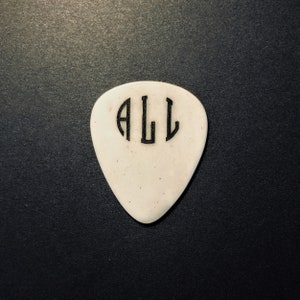 May include: White guitar pick with black lettering that says "ALL" in a circle.