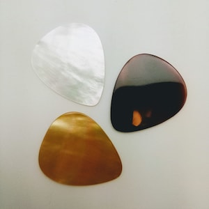 May include: Three guitar picks made of different materials: white, brown, and gold.