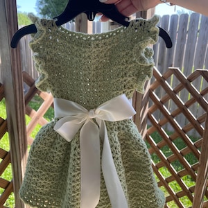 May include: A green crocheted baby dress with a white satin ribbon tied around the waist.