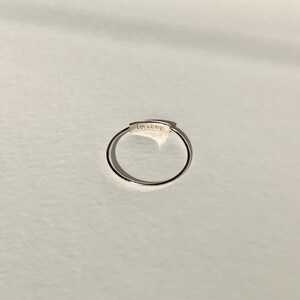 May include: A silver ring with a thin band and a rectangular inscription that reads "lovebug".