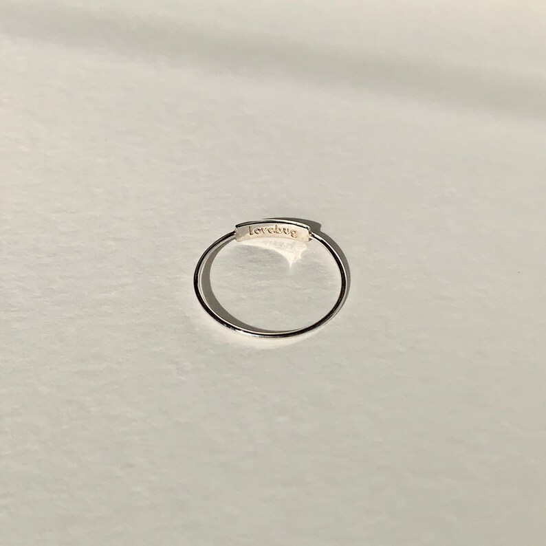 May include: A silver ring with a thin band and a rectangular inscription that reads "lovebug".