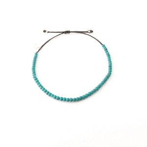 May include: A turquoise beaded bracelet with a brown cord.