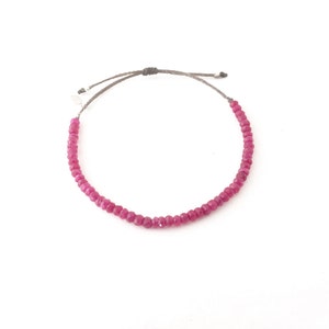 May include: A pink gemstone bracelet with a gray cord and a silver clasp.