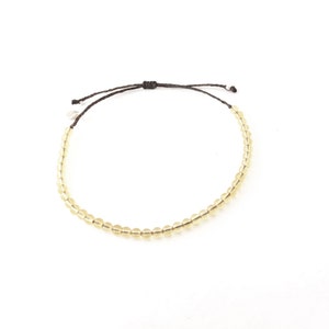 May include: A simple bracelet with a brown cord and small, light yellow beads.