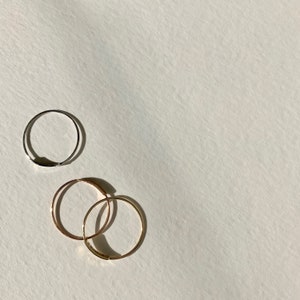 May include: Three simple hoop earrings, two gold and one silver, on a white background.