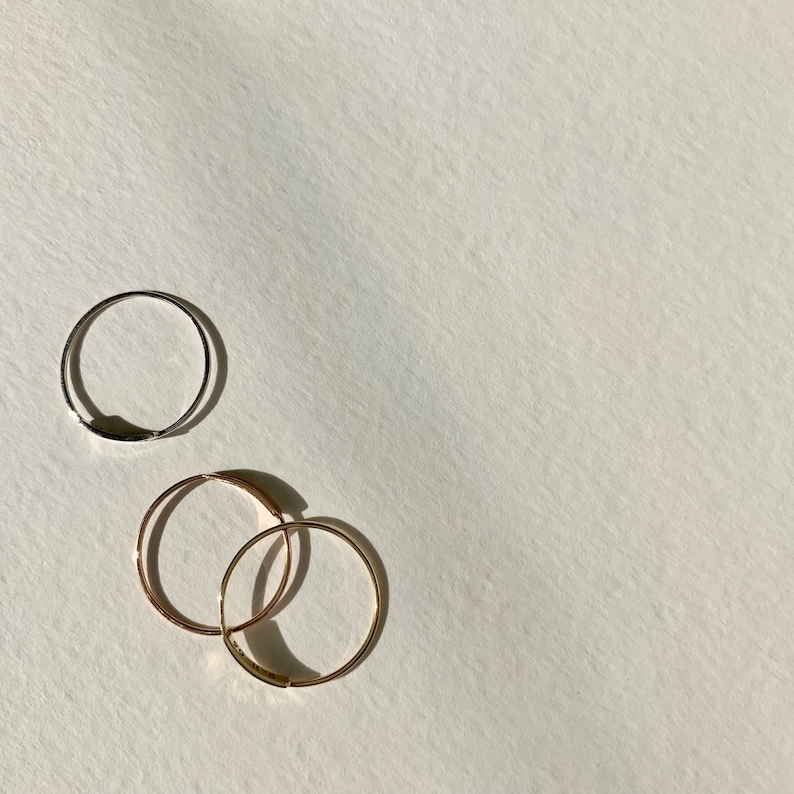 May include: Three simple hoop earrings, two gold and one silver, on a white background.