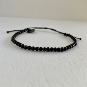 May include: A black beaded bracelet with a simple adjustable cord closure.
