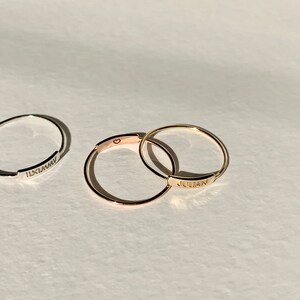 May include: Two thin gold rings with engraved names. The top ring says "JULIAN" and the bottom ring has a small heart symbol.