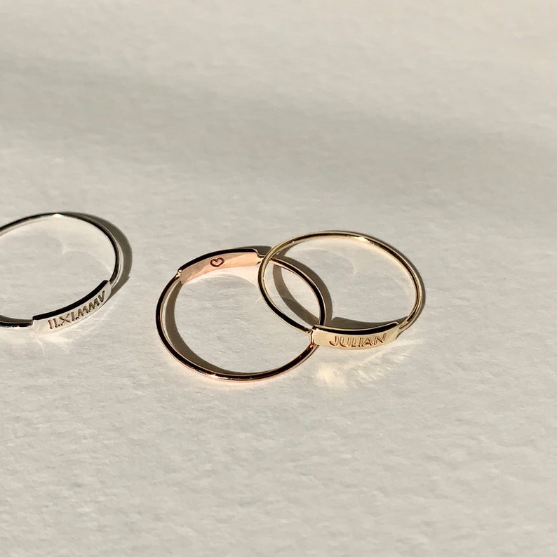 May include: Two thin gold rings with engraved names. The top ring says "JULIAN" and the bottom ring has a small heart symbol.