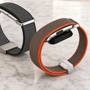 以下が含まれることがあります： 金属製コネクタとマグネット式クラスプを備えた2本のスマートウォッチバンド。1本は黒無地でグレーのテクスチャ織り、もう1本は茶色のテクスチャ織りで鮮やかなオレンジ色の縁取りが施されています。テキストはALEXIUNIQUE.ETSY.COMと記載されています。