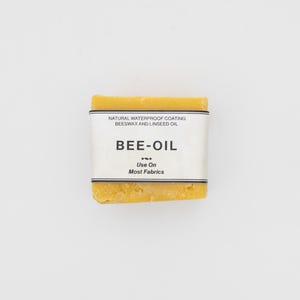 May include: A yellow bar of beeswax and linseed oil "Bee-Oil" for waterproofing most fabrics. The label reads "Natural Waterproof Coating Beeswax and Linseed Oil Bee-Oil Use On Most Fabrics".