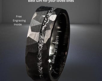 May include: A black tungsten carbide ring featuring a faceted outer surface and a central textured inlay. The interior of the band is engraved with the text Olivia 27.01.2019. The image includes the text Guarenteed Genuine Tungsten Carbide Ring.