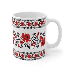 May include: White ceramic mug featuring a floral design in red and black. The design includes stylized flowers and leaves, with a black border at the top and bottom. The mug has a white handle.