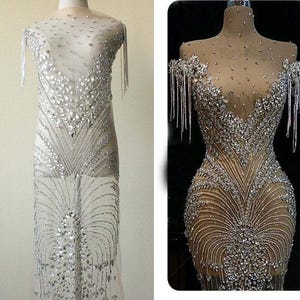 May include: A sheer, beaded dress with a V-neckline and long sleeves. The dress is covered in rhinestones and has a fringe detail on the sleeves.