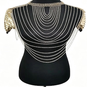 May include: A gold-toned body chain necklace featuring multiple draped silver-colored chains across the chest. The piece includes a decorative collar section and shoulder epaulets constructed from overlapping metallic scale-like plates.