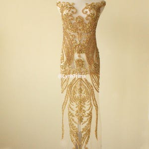 Pode incluir: Aplique de contas douradas com um design floral em um tecido de malha transparente. O aplique é perfeito para adicionar um toque de glamour a qualquer peça de roupa.