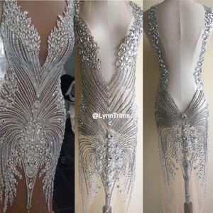 Può includere: Un'applicazione in tessuto trasparente, con perline e paillettes, con scollo a V e apertura sul retro. L'applicazione è realizzata con perline e paillettes argentate e presenta un design delicato e fluido. L'applicazione è perfetta per aggiungere un tocco di glamour a qualsiasi capo.