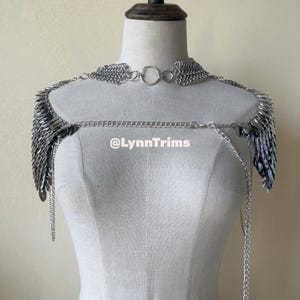 May include: Silver chainmail shoulder piece with a collar, shoulder drapes, and a chest chain. The piece is displayed on a mannequin. The text "@LynnTrims" is visible on the chest.