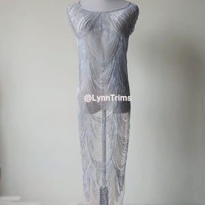 Puede incluir: Un vestido de malla plateada con un diseño en capas. El vestido es transparente y tiene un corte holgado. El vestido se muestra en un maniquí.