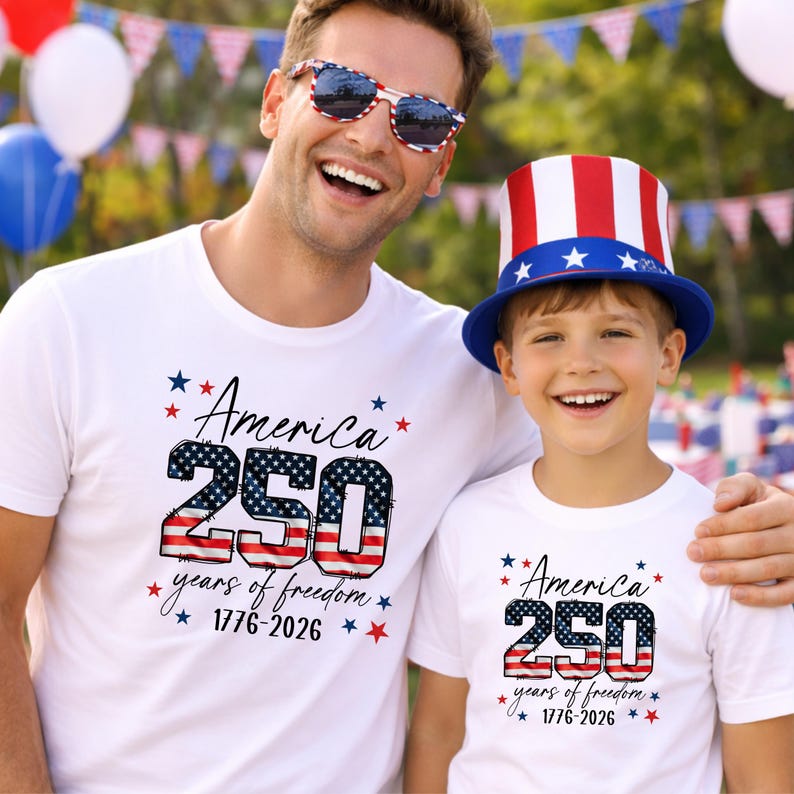 May include: White t-shirts with the text "America 250 years of freedom 1776-2026" in red, white, and blue. One person wears sunglasses with a red, white, and blue pattern. A child wears a red, white, and blue top hat.
