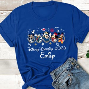 May include: Royal blue t-shirt featuring Disney characters in portholes. The design includes Mickey Mouse, Donald Duck, and Minnie Mouse. The text reads "Disney Destiny 2026" and "Emily".