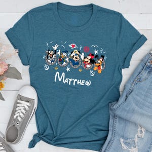 May include: Teal t-shirt featuring a graphic of Disney characters in sailor outfits. The characters are in portholes with anchors and stars. The name "Matthew" is written in white script below the graphic.