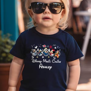May include: Navy blue t-shirt featuring Disney characters in sailor outfits. The shirt has the text "Disney Magic Cruise" and a personalized name. The design includes Mickey Mouse, Minnie Mouse, and other characters.