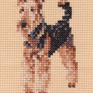 Pode incluir: Padrão de ponto cruz de um cão terrier marrom e preto com peito branco. O cão está em pé sobre um fundo bege.