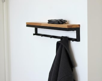 Könnte beinhalten: Wandregal mit einer Oberseite aus Naturholz und einem schwarzen Metallrahmen. Unter dem Regal befindet sich eine Reihe von Haken. Ein dunkelgrauer Mantel hängt an einem der Haken, und ein Paar graue Handschuhe liegt auf dem Regal.