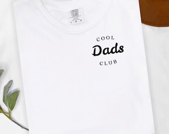 May include: White t-shirt with black text that reads "Cool Dads Club".