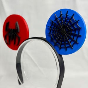 May include: Spider-Man themed mouse ears. The ears are red and blue circles with a black spider and spiderweb design. The headband is black with a clear plastic center.