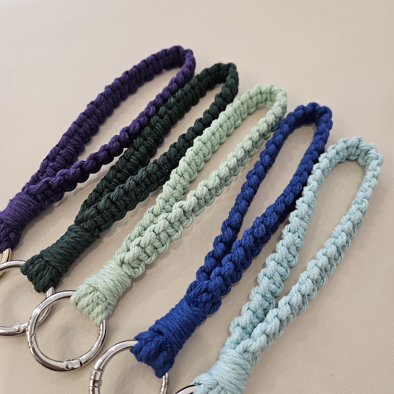 Pu&ograve; includere: Primo piano di cinque cordini macram&egrave; in vari colori: viola, verde scuro, verde chiaro, blu e azzurro. Ogni cordino ha un anello metallico color argento alla base. Il macram&egrave; &egrave; intrecciato fittamente, creando un aspetto strutturato.