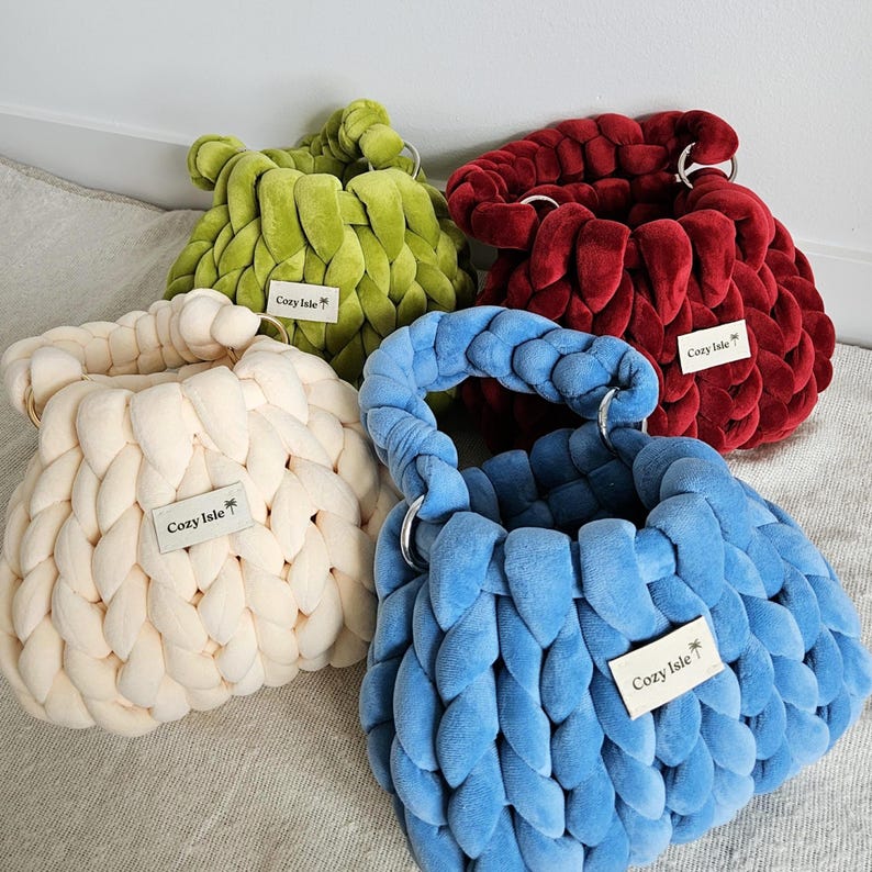 May include: Four crocheted handbags in different colors: cream, green, red, and blue. Each bag has a  "Cozy Isle" label attached.