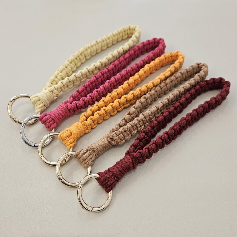 Pu&ograve; includere: Una collezione di sei portachiavi da polso in macram&egrave; in vari colori. I portachiavi presentano un design intrecciato e sono nelle tonalit&agrave; di beige, rosa, arancione, marrone chiaro e bordeaux. Ogni portachiavi ha un anello in metallo color argento.
