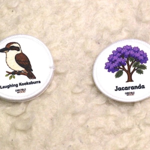 May include: Two circular white patches featuring illustrations. The left patch shows a brown and white Laughing Kookaburra bird on a branch with the text Laughing Kookaburra and Double Wood. The right patch shows a purple Jacaranda tree with the text Jacaranda and Double Wood.
