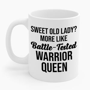 May include: White ceramic mug with a curved handle. The mug features black text that reads "SWEET OLD LADY? MORE LIKE Battle-Tested WARRIOR QUEEN."