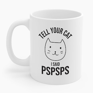 Puede incluir: Taza de cerámica blanca con un gráfico de cara de gato negro y el texto "TELL YOUR CAT I SAID PSPSPS". La taza tiene un asa curva y está diseñada para bebidas calientes.