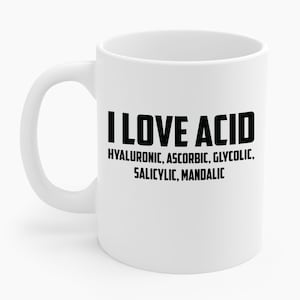 Op de afbeelding: Witte keramische mok met een gebogen handvat. De mok heeft de tekst "I LOVE ACID" in vette zwarte letters, gevolgd door een lijst met zuren: hyaluronzuur, ascorbinezuur, glycolzuur, salicylzuur en mandelzuur.