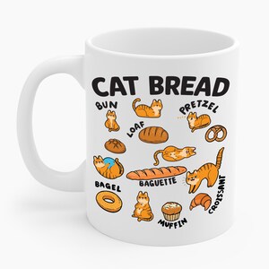 Puede incluir: Taza de cerámica blanca con la inscripción "CAT BREAD" en negro, con ilustraciones de gatos con forma de diferentes tipos de pan, incluyendo un bollo, pan de molde, bagel, baguette, pretzel, croissant y muffin.