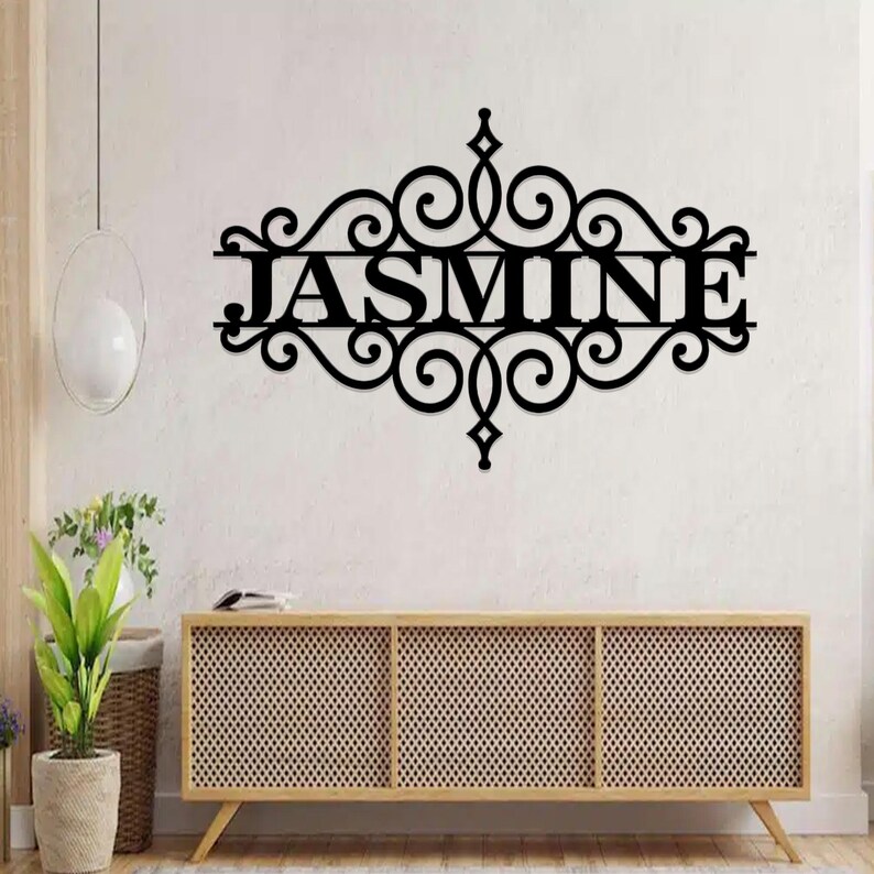 Pu&ograve; includere: Decorazione da parete in metallo nero con un design a volute decorative e il nome "JASMINE" al centro.