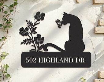 Könnte beinhalten: Ein schwarzes Metall-Wandschild mit der Silhouette einer Katze, die neben einem Blumenstängel sitzt und einen Schmetterling betrachtet. Unter der Katze und den Blumen befindet sich eine rechteckige Platte mit dem Text 502 HIGHLAND DR.