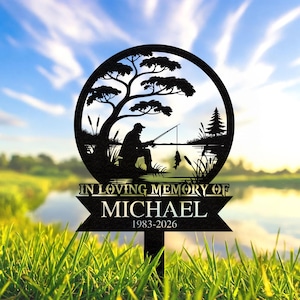 May include: Black metal memorial garden stake with a silhouette of a person fishing by a lake, framed by a circle with a tree and reeds. The text reads "IN LOVING MEMORY OF MICHAEL 1983-2026".