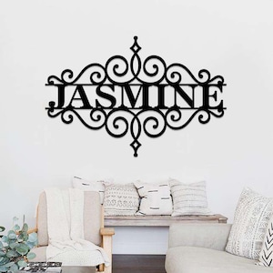 Può includere: Decorazione da parete in metallo nero con un design a volute decorative e il nome "JASMINE" al centro.
